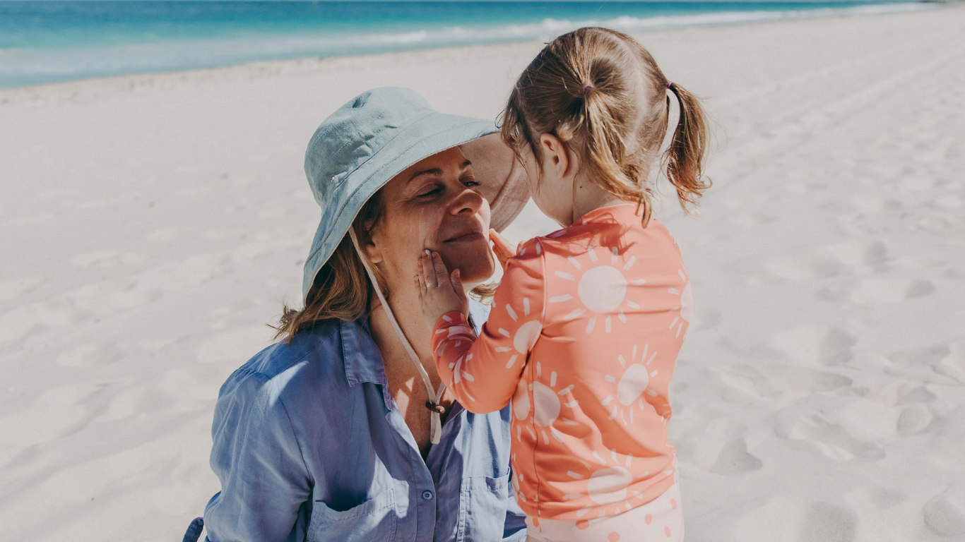 Child applying sunscreen to woman’s face on the beach