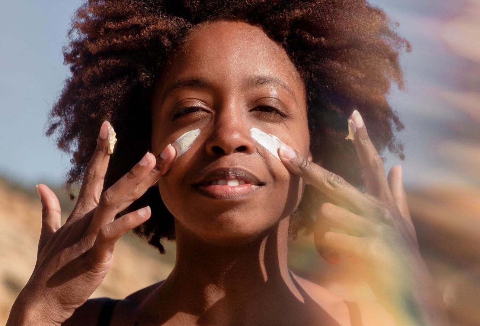 Beautiful black woman putting zinc oxide on her cheeks