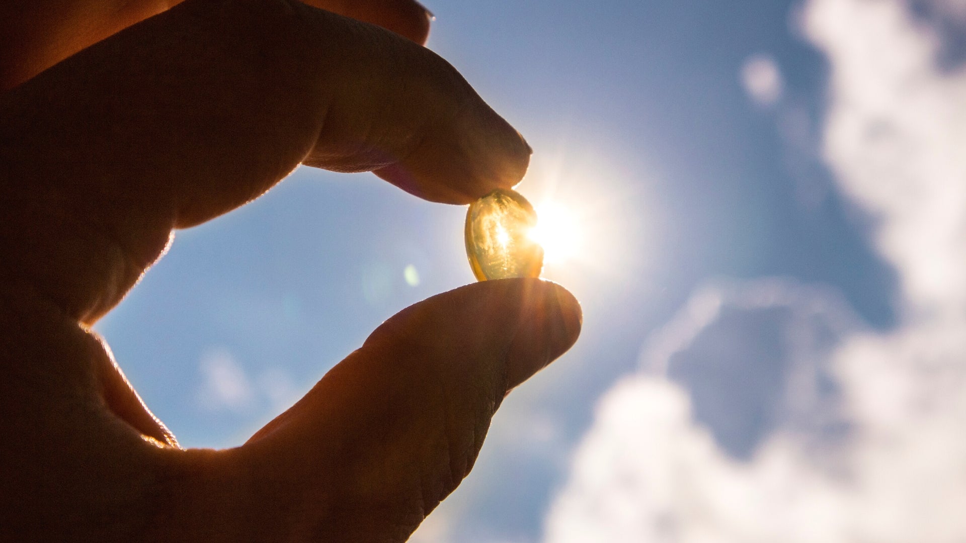 Two fingers holding up a vitamin d capsule against the sun