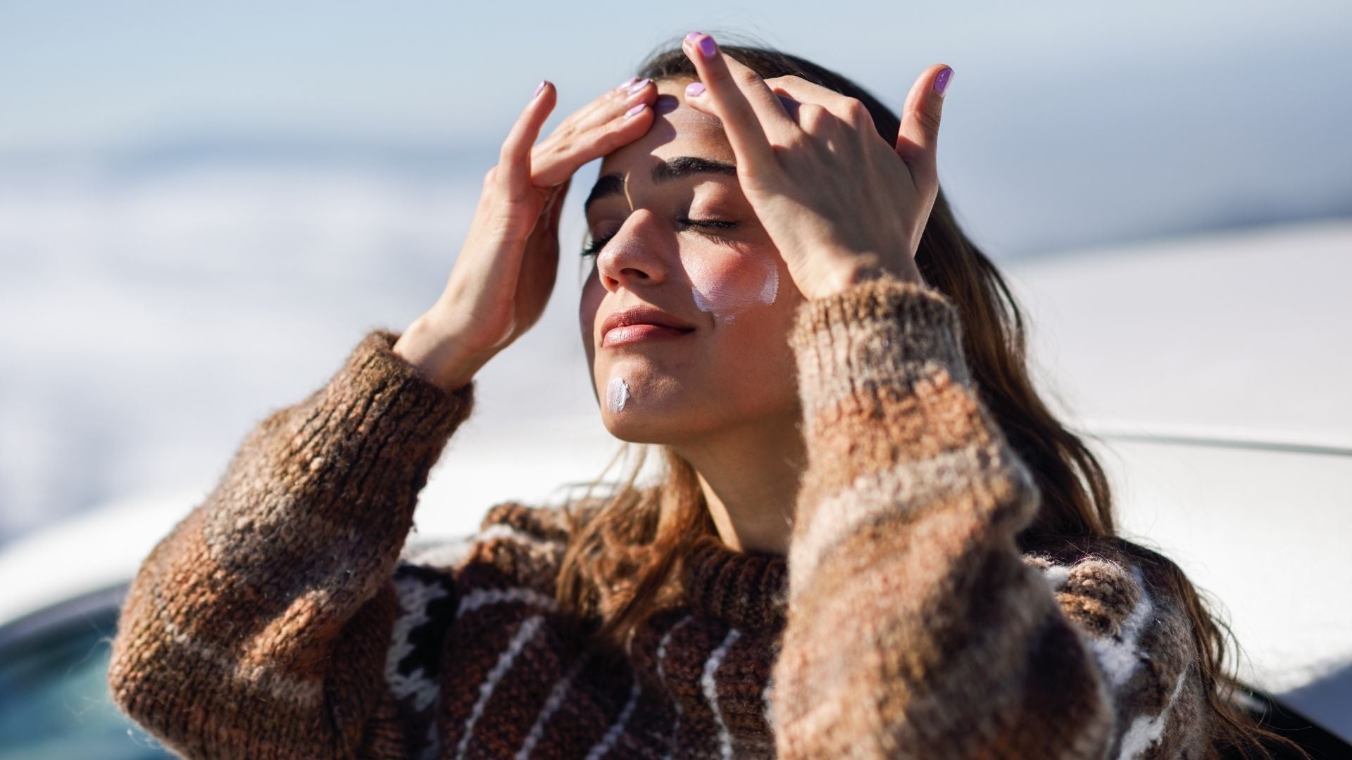 Woman in a brown jumper applying sunscreen in winter